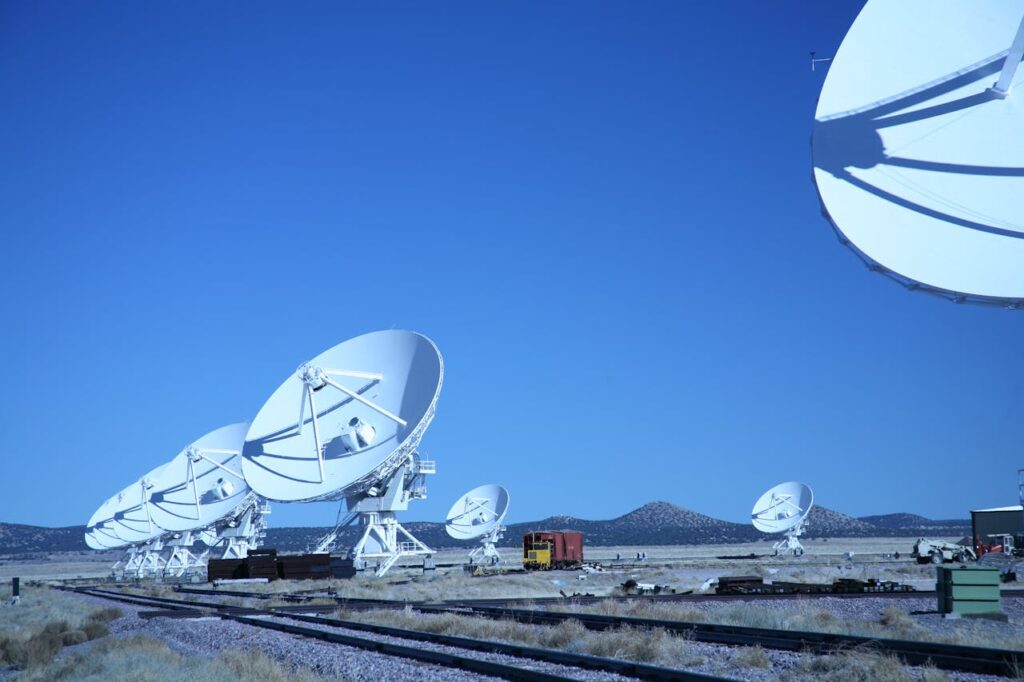 pexels-photo-13866732 Multiple satellite dishes aligned in a field against a vibrant blue sky, showcasing modern communication technology.